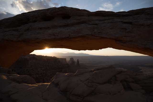 A natural sandstone arch frames the setting sun over a vast desert landscape.