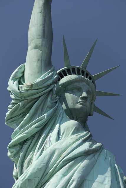 A copper statue depicts a woman wearing a crown and flowing robes, with an arm raised.