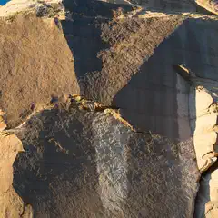 A rock formation featuring large stone sections with varying shades of brown and tan hues set against a bright blue sky.