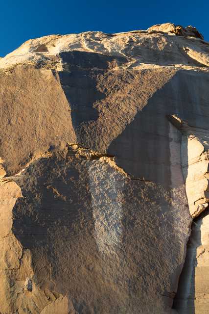 A rock formation featuring large stone sections with varying shades of brown and tan hues set against a bright blue sky.