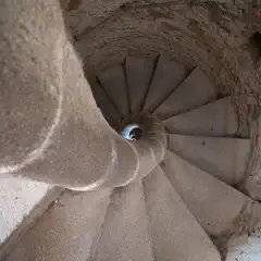 A spiral staircase ascends through a circular stone structure, viewed from above.