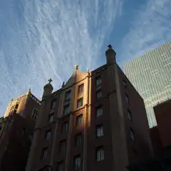 A Gothic-style building with two towers and a central spire rises against a blue sky. A modern glass skyscraper stands in the background.