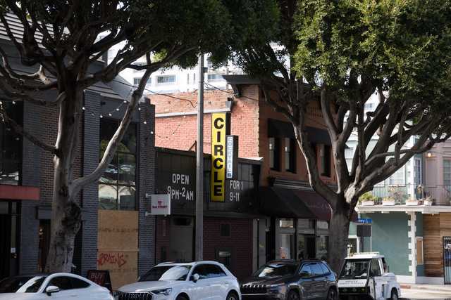A city street lined with trees and buildings, featuring a bar sign that reads "CIRCLE".