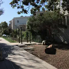 A paved path leads through a park with trees and shrubs, surrounded by residential buildings.