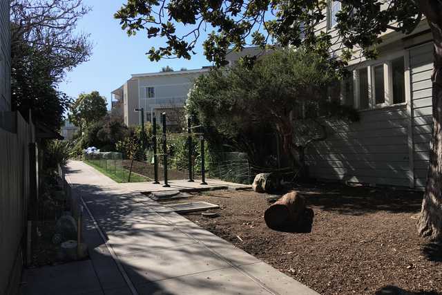 A paved path leads through a park with trees and shrubs, surrounded by residential buildings.