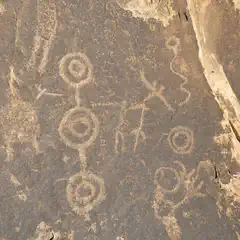An ancient petroglyph panel is depicted on a rock face, featuring circular designs and other symbols.
