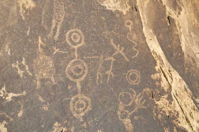 An ancient petroglyph panel is depicted on a rock face, featuring circular designs and other symbols.
