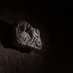 A carved stone relief depicting a figure is mounted on a brick wall, illuminated against a dark background.