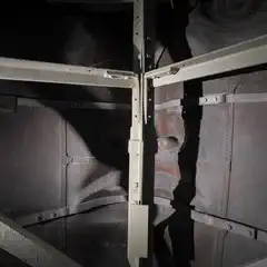 A metal structure with a face carved into it, partially obscured by bars and shadows.