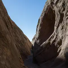 A narrow canyon carved between two towering sandstone formations under a clear blue sky.