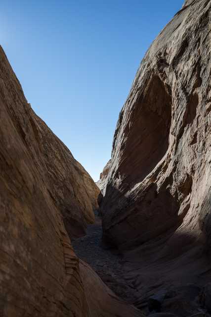 A narrow canyon carved between two towering sandstone formations under a clear blue sky.