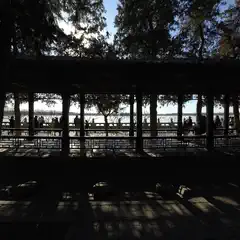A covered walkway with a series of columns frames people standing along a body of water.