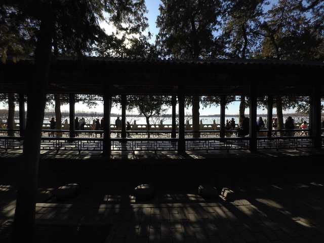 A covered walkway with a series of columns frames people standing along a body of water.