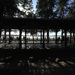 A covered walkway with a series of columns frames people standing along a body of water.