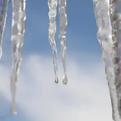 Several icicles hanging from an unseen structure, with the sky visible through them.