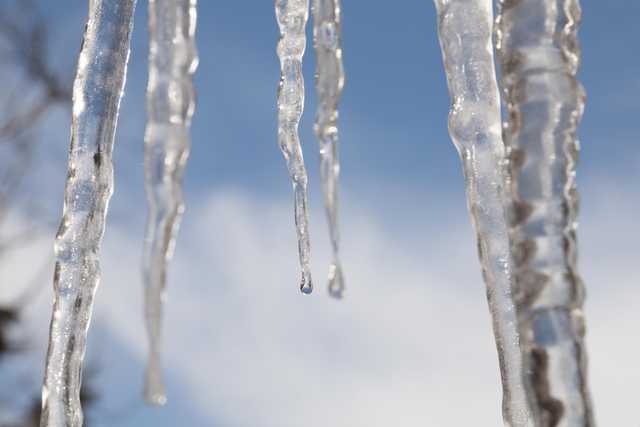 Several icicles hanging from an unseen structure, with the sky visible through them.