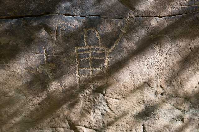 A section of rock art features a geometric pattern composed of squares, etched into the surface.