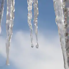 Several icicles hanging from an unseen structure, with the sky visible through them.