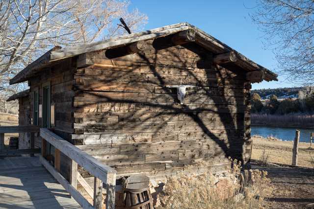 A weathered wooden cabin stands alongside a body of water, with a prominent skull mounted on its side.