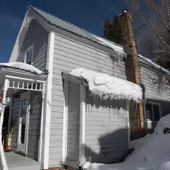 A white house with snow on its roof and melting icicles hanging off the eaves.