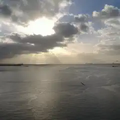 Sunlight piercing through clouds over calm water with distant boats and birds.