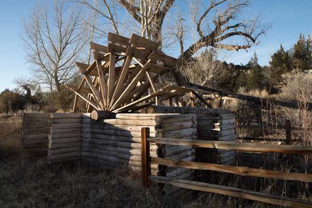 An old wooden waterwheel is situated behind a log fence, with its spokes and paddles visible.