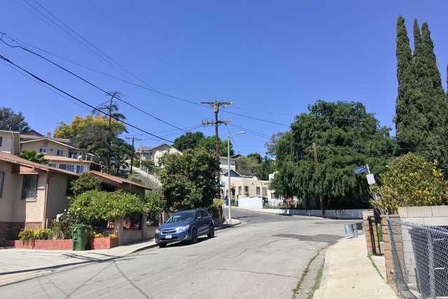 A street is lined by trees and houses with a blue car parked on the side of the road.