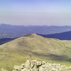 A rocky landscape atop a mountain peak, with distant mountains and a clear sky.