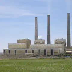 An industrial building with three tall smokestacks is visible beyond a field of green grass.