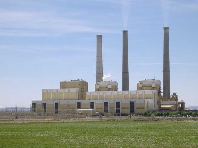 An industrial building with three tall smokestacks is visible beyond a field of green grass.