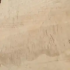 A beige stone wall features numerous small, shallow carvings, likely created using a sharp tool or rock.