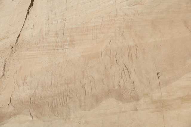 A beige stone wall features numerous small, shallow carvings, likely created using a sharp tool or rock.