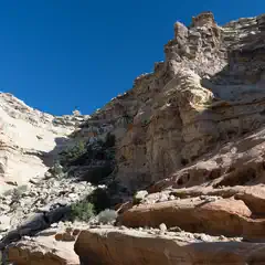 A rocky landscape features towering cliffs set against a clear blue sky.