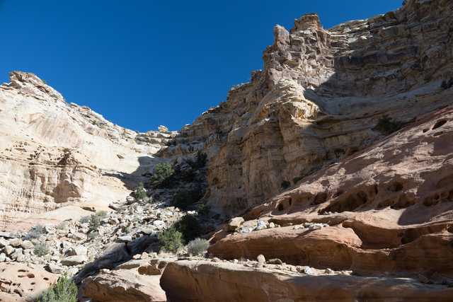 A rocky landscape features towering cliffs set against a clear blue sky.