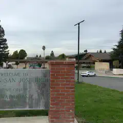 A large building with a covered entrance is visible behind a red brick sign that reads "Welcome to Mission San Jose High".