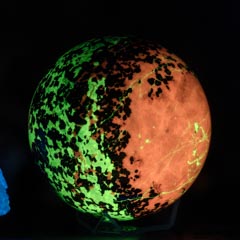 A glowing sphere with green and red patterns, surrounded by blue and yellow luminescent minerals, against a dark background.