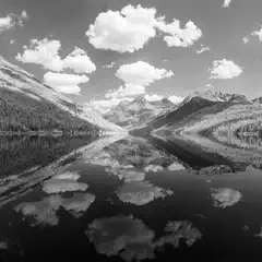 A serene mountain lake with a clear reflection of clouds and mountains on its surface.