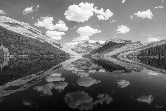 A serene mountain lake with a clear reflection of clouds and mountains on its surface.