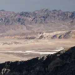 A rocky outcropping dominates the foreground, set against a backdrop of arid terrain featuring a vast expanse of dry lakebed and distant mountains.