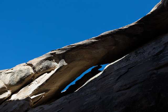 An arch-like rock formation sits atop a steep slope against a clear blue sky.