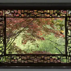 A rectangular window with an ornate black frame contains a view of trees with red and green foliage.