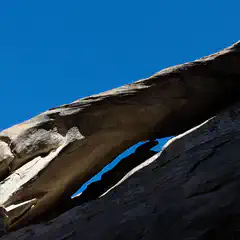 An arch-like rock formation sits atop a steep slope against a clear blue sky.