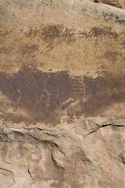 A rock face features a horizontal band of dark brown and yellow hues that gradually lightens toward the top, set against a lighter background.