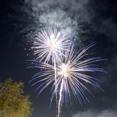 Two fireworks burst in the night sky, emitting white and blue sparks.