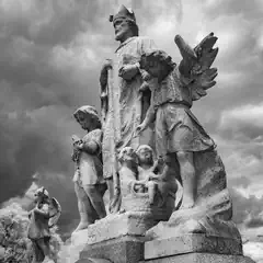 A stone monument features several human figures, including a crowned central figure and an angel with outstretched wings.