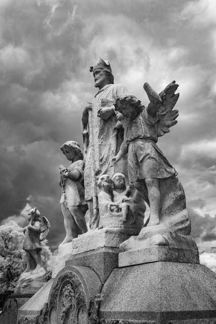 A stone monument features several human figures, including a crowned central figure and an angel with outstretched wings.