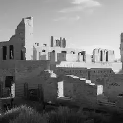 A large stone building in disrepair with missing roofs and walls, surrounded by overgrown vegetation.