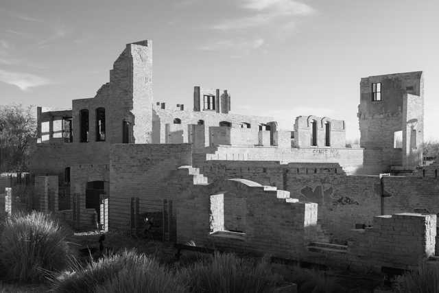 A large stone building in disrepair with missing roofs and walls, surrounded by overgrown vegetation.
