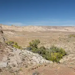 A desert landscape featuring rocky outcrops and scrubby vegetation stretches towards distant mountains under a clear blue sky.