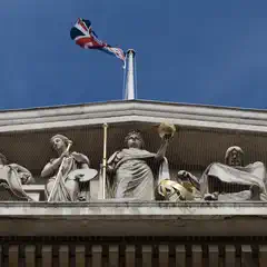 A Union Jack flies above a frieze of classical stone statues on a building facade.